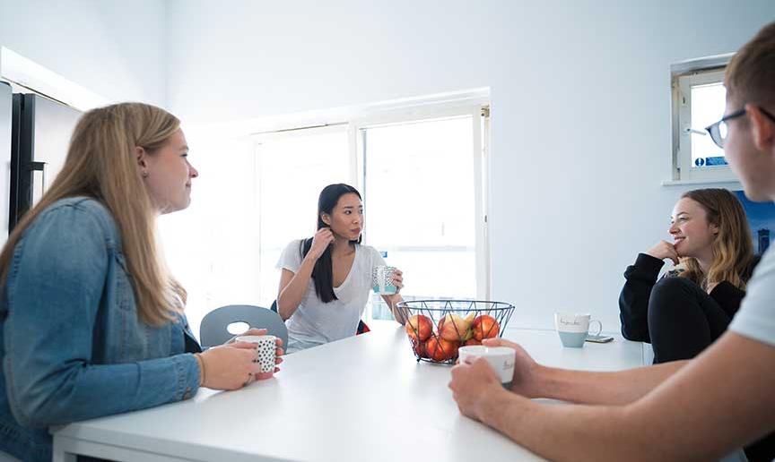 Four students sit in their Sanctuary Students flat kitchen with a hot drink.