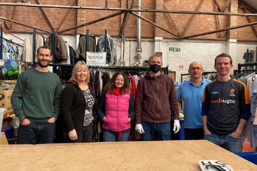 Sanctuary's finance team volunteering for St Richard's Hospice, standing in front of rails of donated clothes in St Richard's donation warehouse.