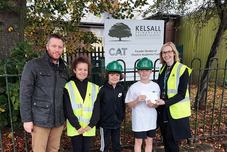 Headteacher and pupils hold up voucher wearing hard hats