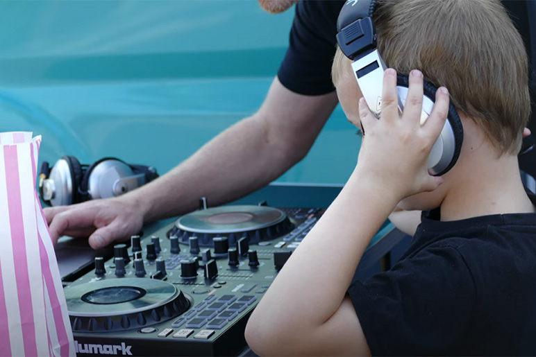 Stock image of child wearing headphones looking at DJ equipment