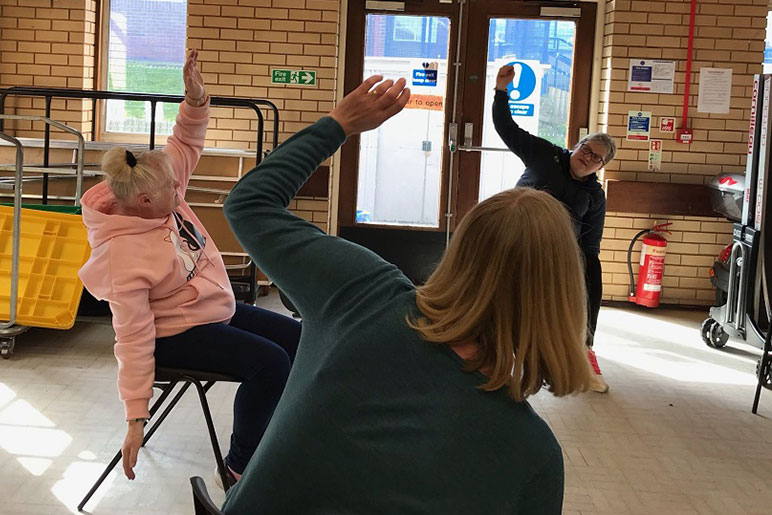 An instructor gets people moving and stretching in a gentle chair yoga session.