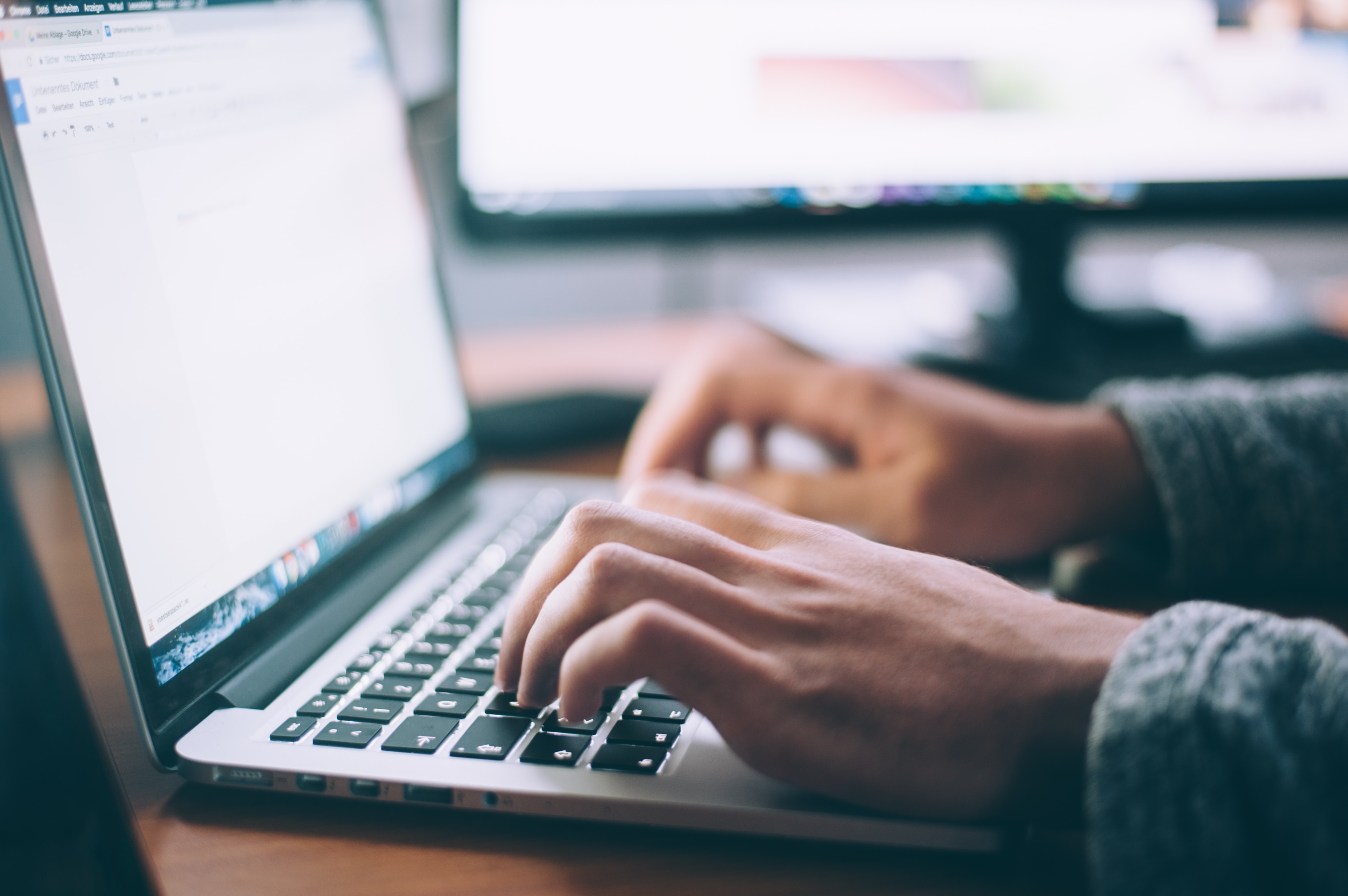 Hands typing on a laptop with a second monitor in the background