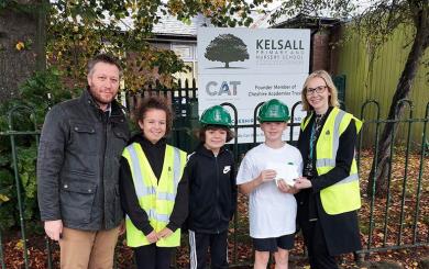 Headteacher and pupils hold up voucher wearing hard hats