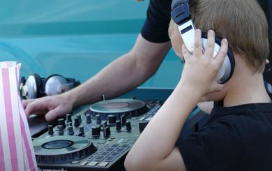 Stock image of child wearing headphones looking at DJ equipment