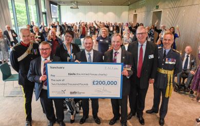 A large group of people standing in a room raising their glasses in celebration. In the forefront of the picture are six males and one female holding a large cheque for £200,000 from Sanctuary to the Armed Forces charity. Some of the men are wearing military medals.