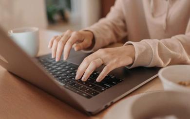 Stock image of a person typing on the keyboard of a laptop that sits on a wooden table