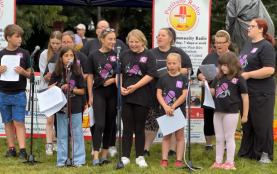 A group of people of different genders and ages that make up a choir performing at an outdoor local event