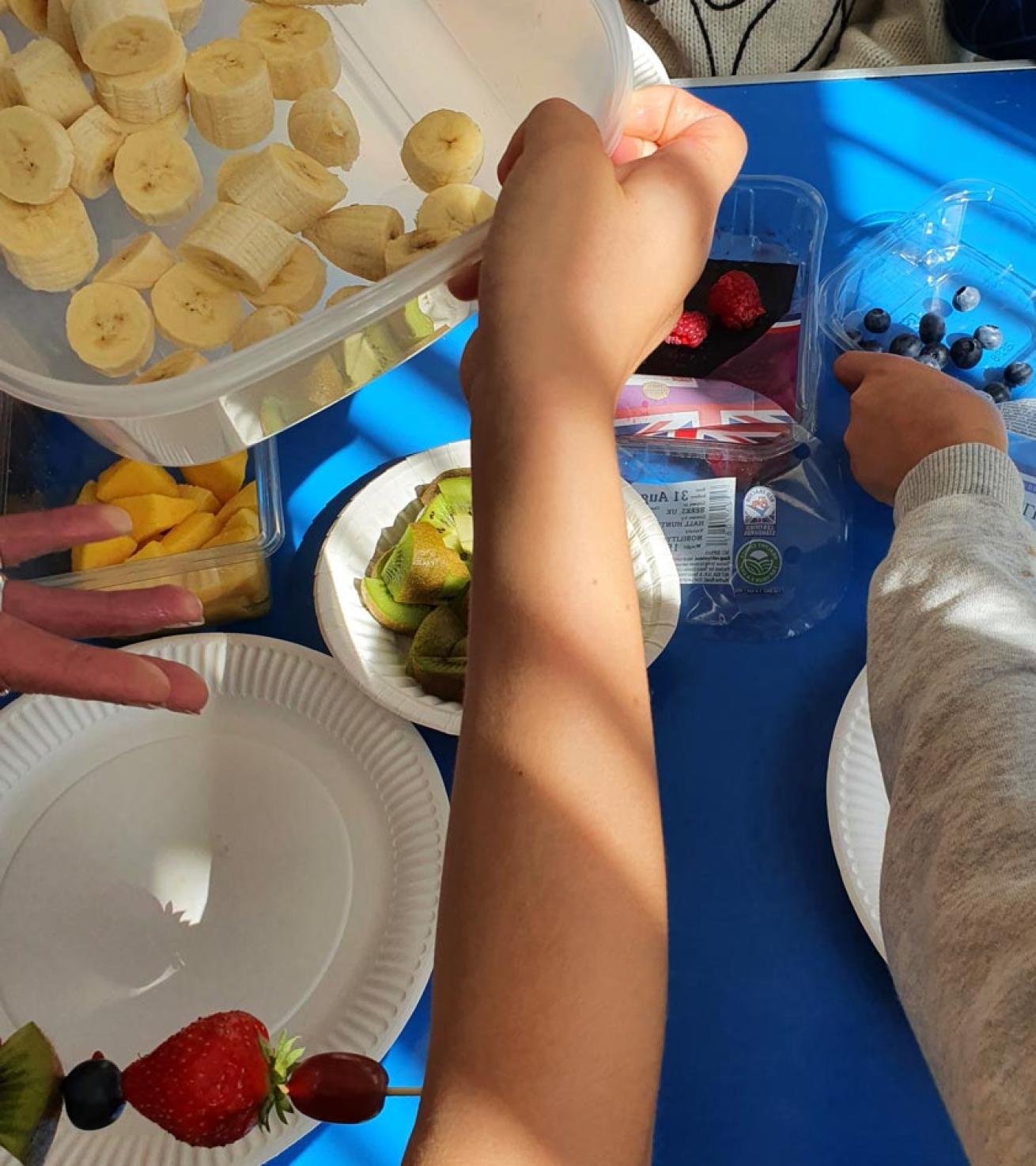 Hands making fruit kebabs