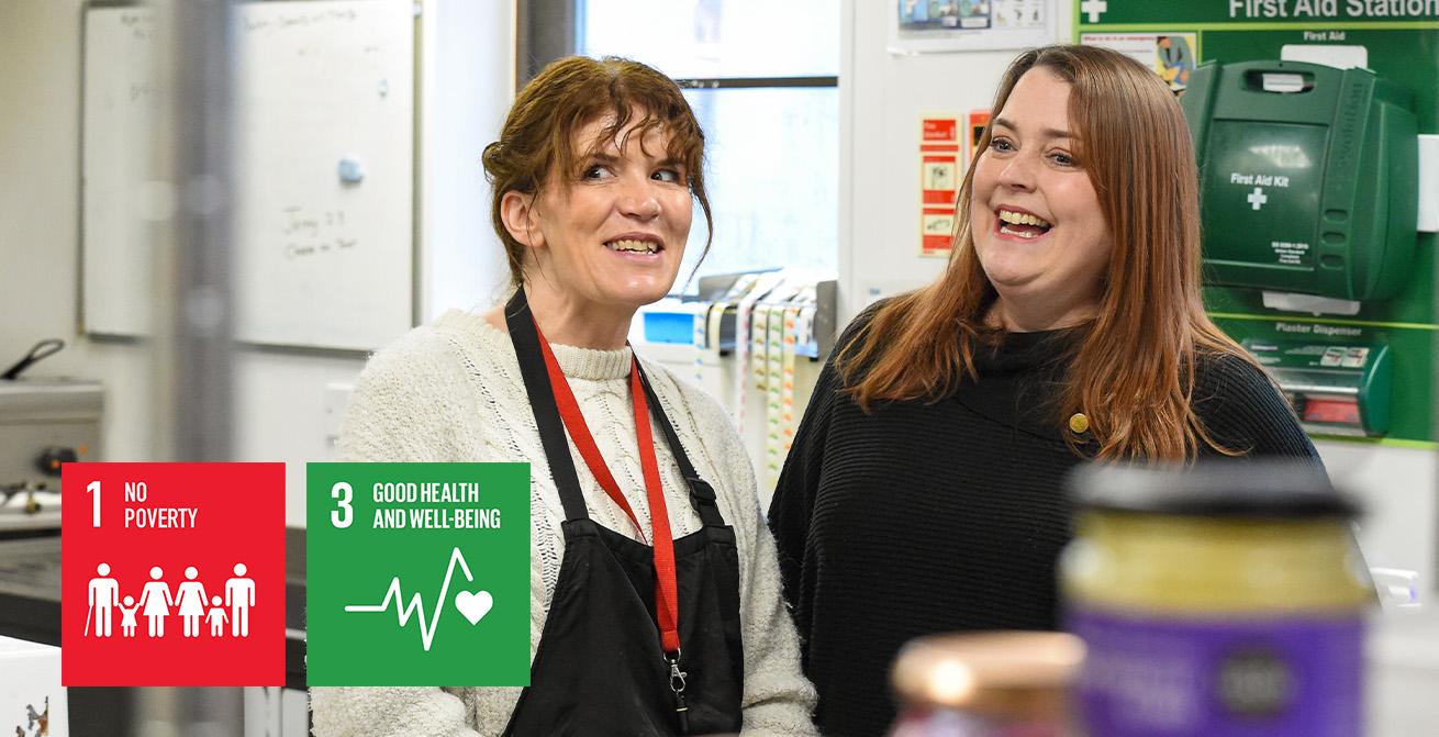 Two women standing in a kitchen in a professional kitchen. The UN icons for 'No Poverty' and 'Good health and well-being' are overlayed on top