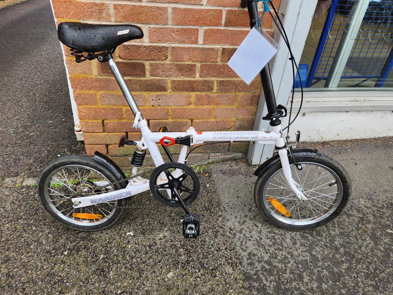 A black and white foldable bike leant up against a brick wall