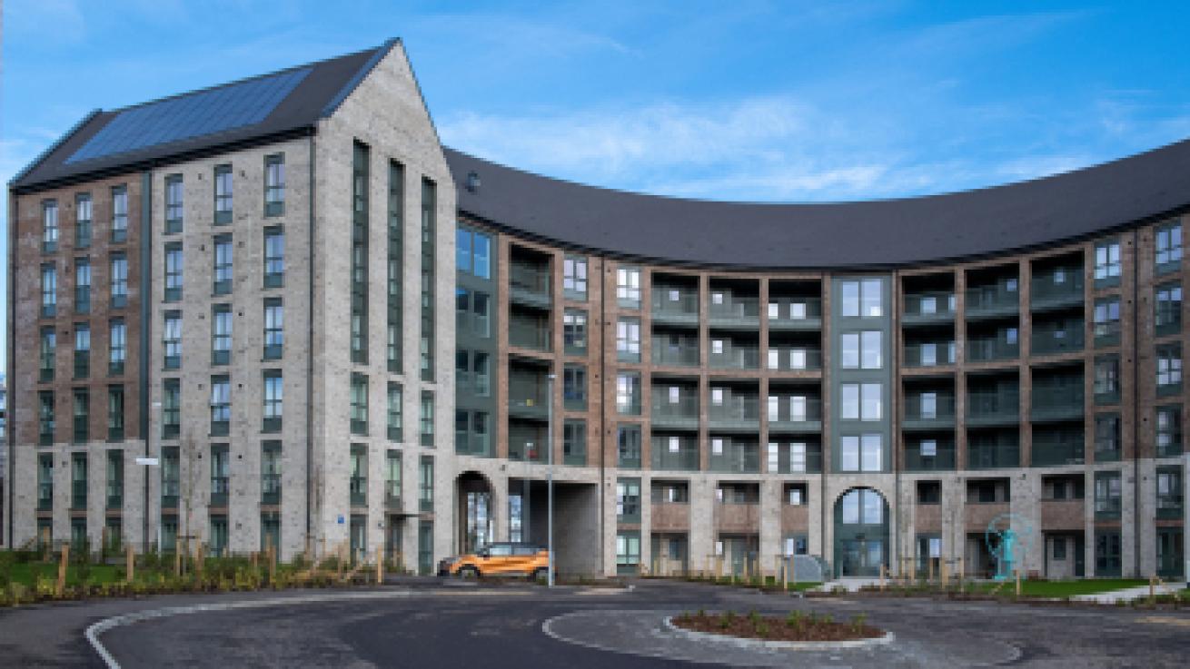 Exterior of a curved block of flats built using grey brick with a roundabout in the foreground