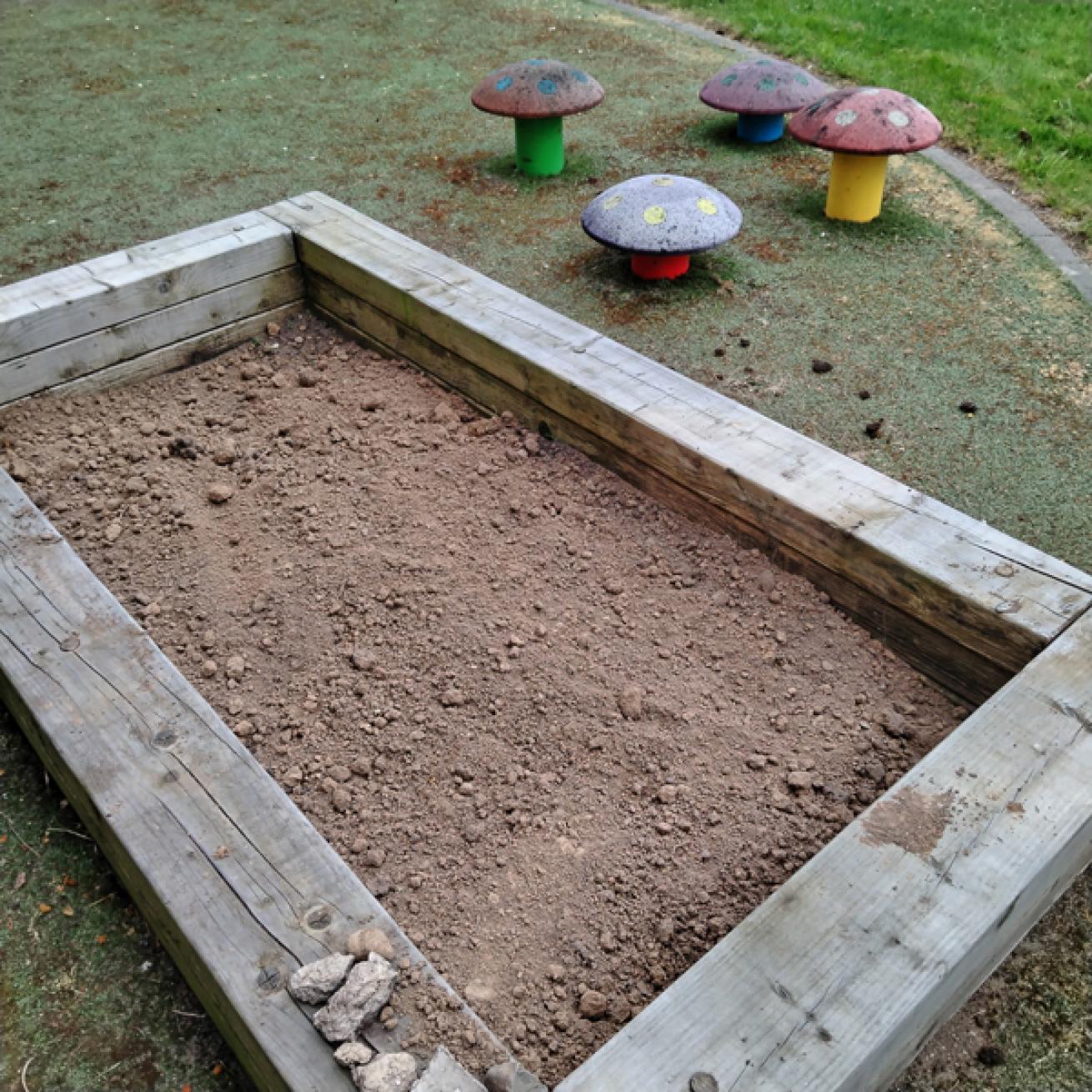 A dirt filled wooden box with several metal toadstools on the side