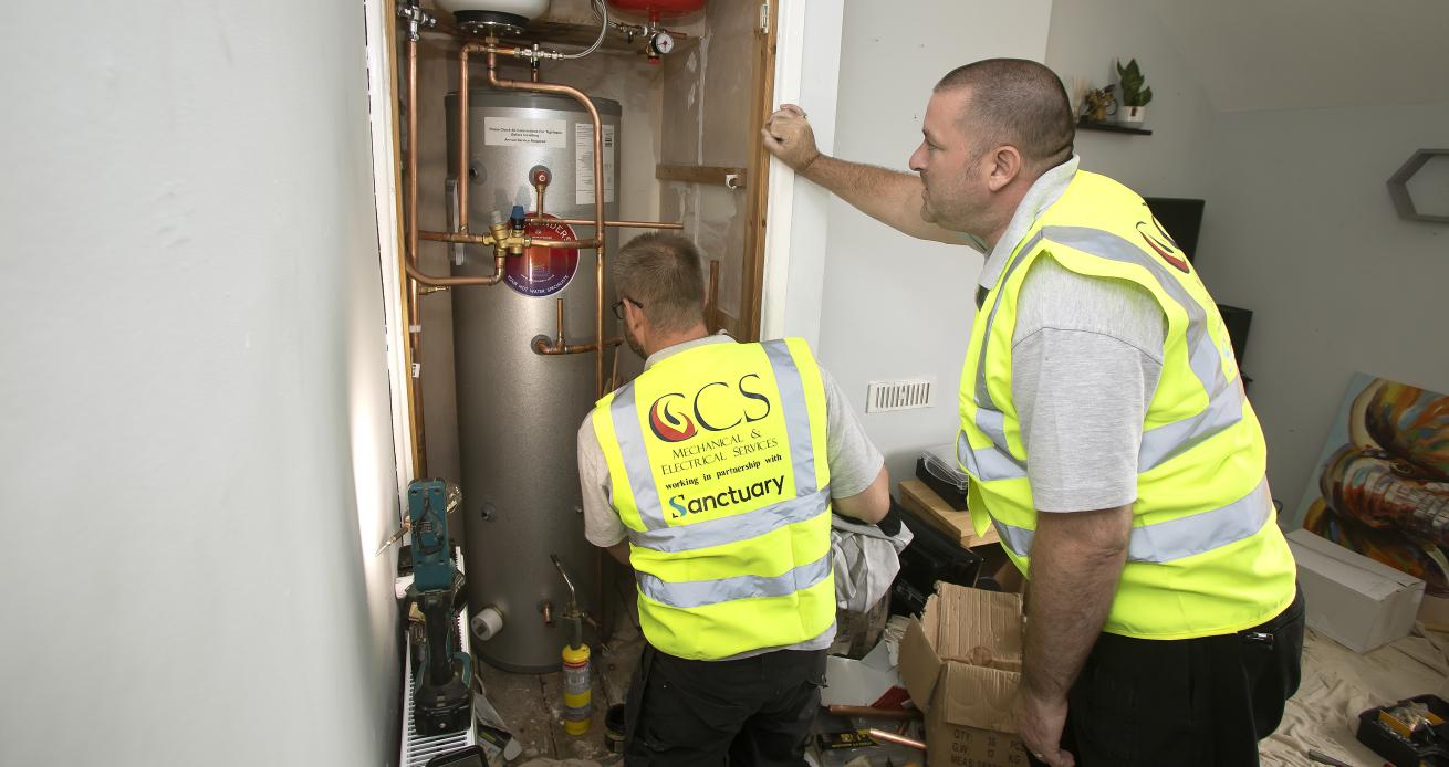 Two men wearing yellow high visibility jackets carrying out maintenance work on a boiler