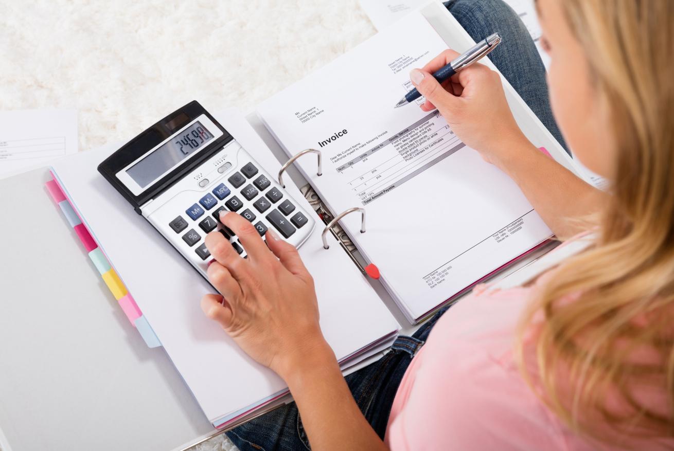 A woman making calculations of a calculator and writing notes in a notepad. 