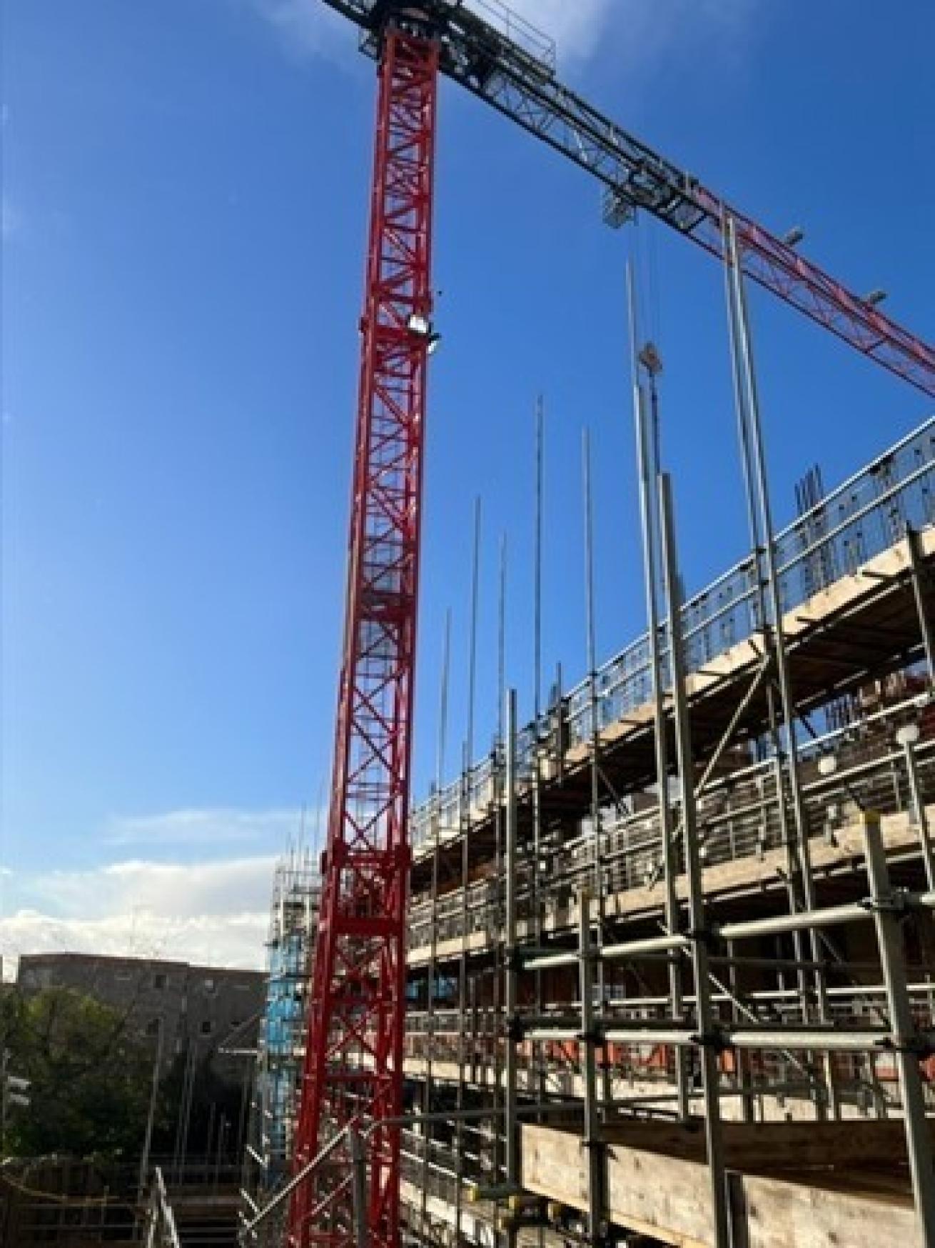 A red construction crane stood next to a building covered in scaffolding