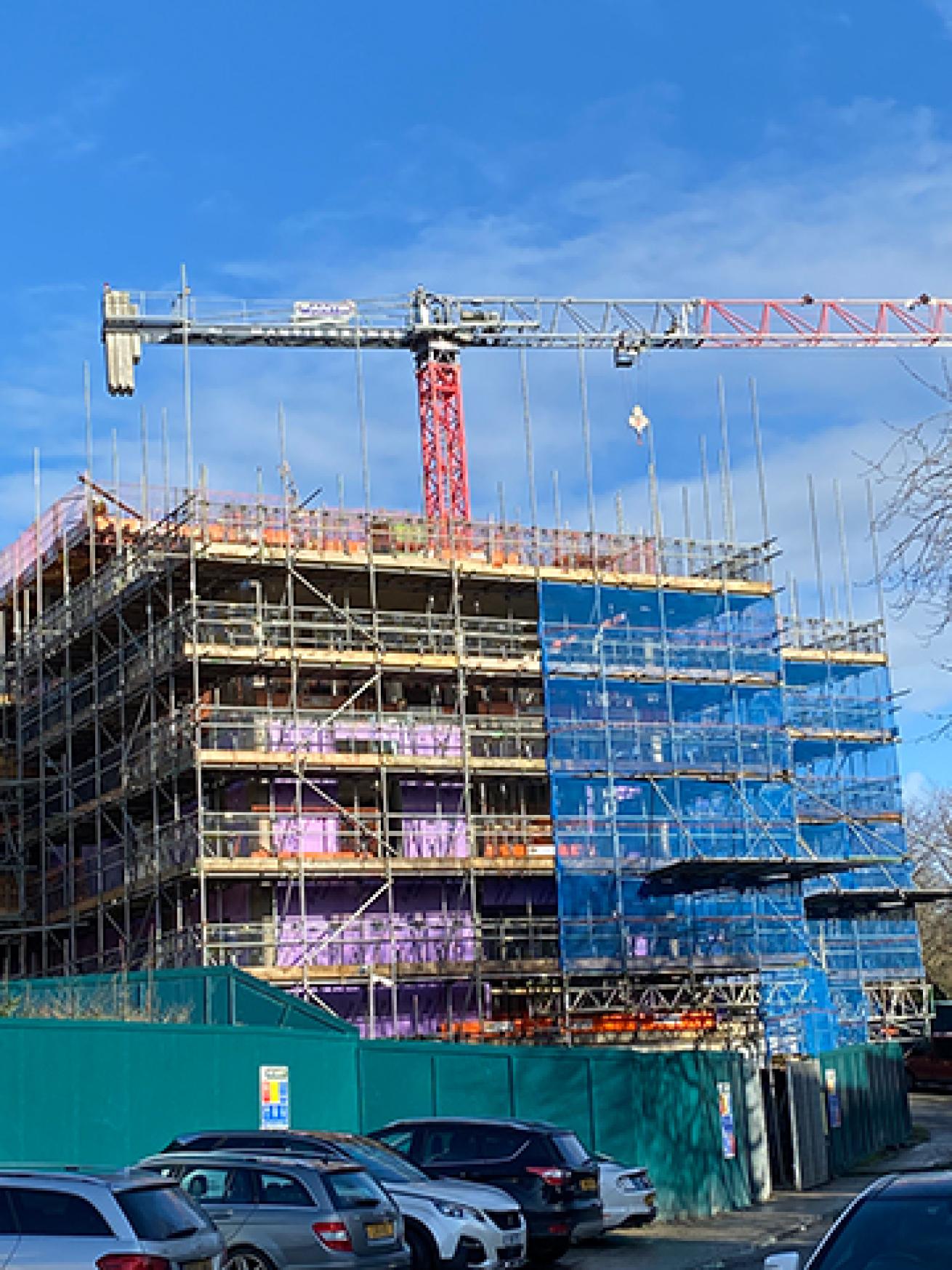 A building site showing a building covered in scaffolding with a construction crane behind