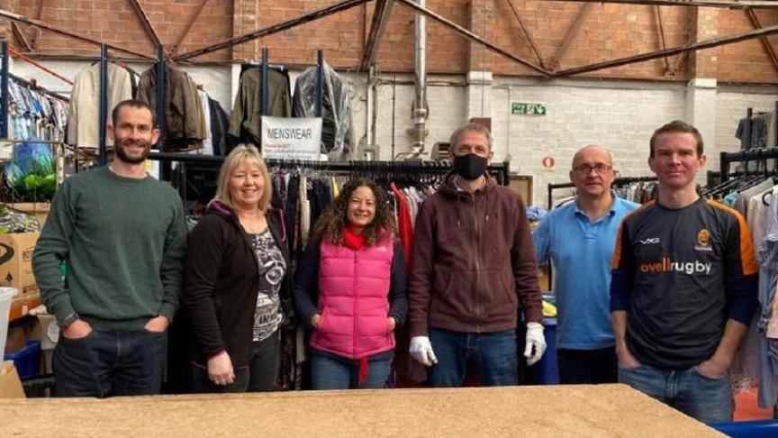 Sanctuary's finance team volunteering for St Richard's Hospice, standing in front of rails of donated clothes in St Richard's donation warehouse.