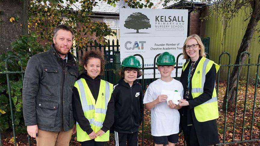 Headteacher and pupils hold up voucher wearing hard hats