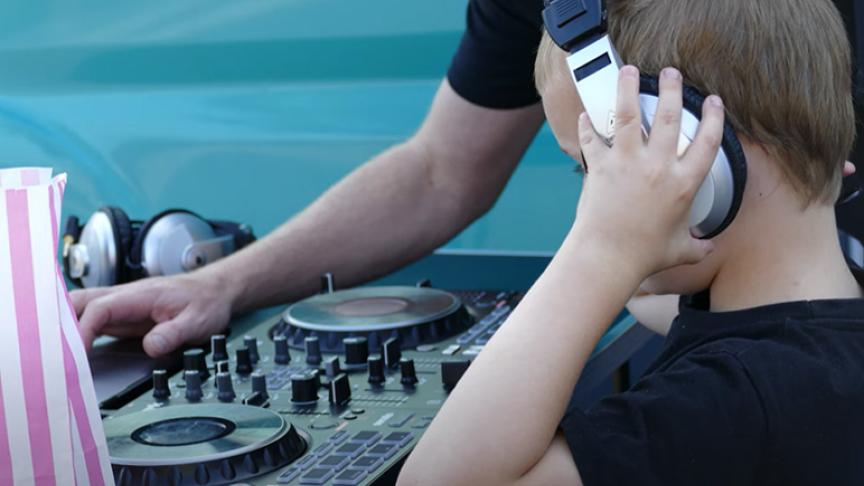 Stock image of child wearing headphones looking at DJ equipment