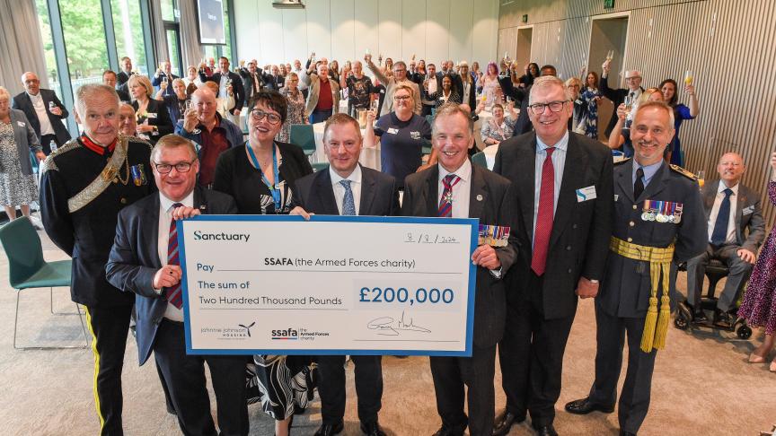 A large group of people standing in a room raising their glasses in celebration. In the forefront of the picture are six males and one female holding a large cheque for £200,000 from Sanctuary to the Armed Forces charity. Some of the men are wearing military medals.