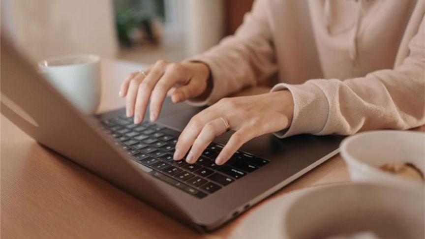 Stock image of a person typing on the keyboard of a laptop that sits on a wooden table