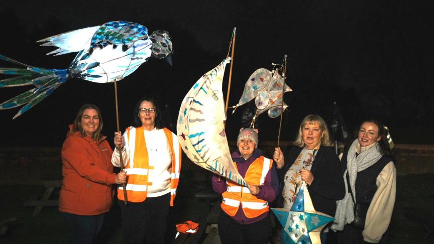 A group of people stood in the dark wearing warm clothes holding their lanterns