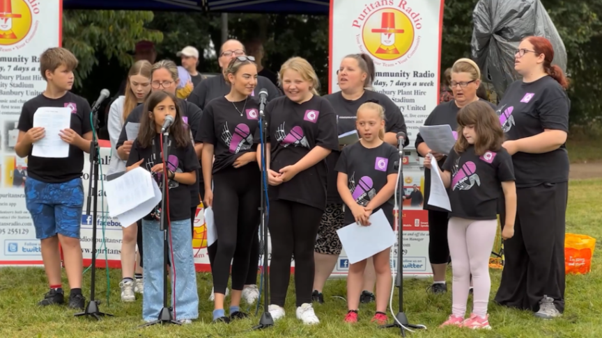 A group of people of different genders and ages that make up a choir performing at an outdoor local event