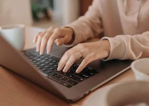 Stock image of a person typing on the keyboard of a laptop that sits on a wooden table