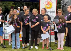 A group of people of different genders and ages that make up a choir performing at an outdoor local event